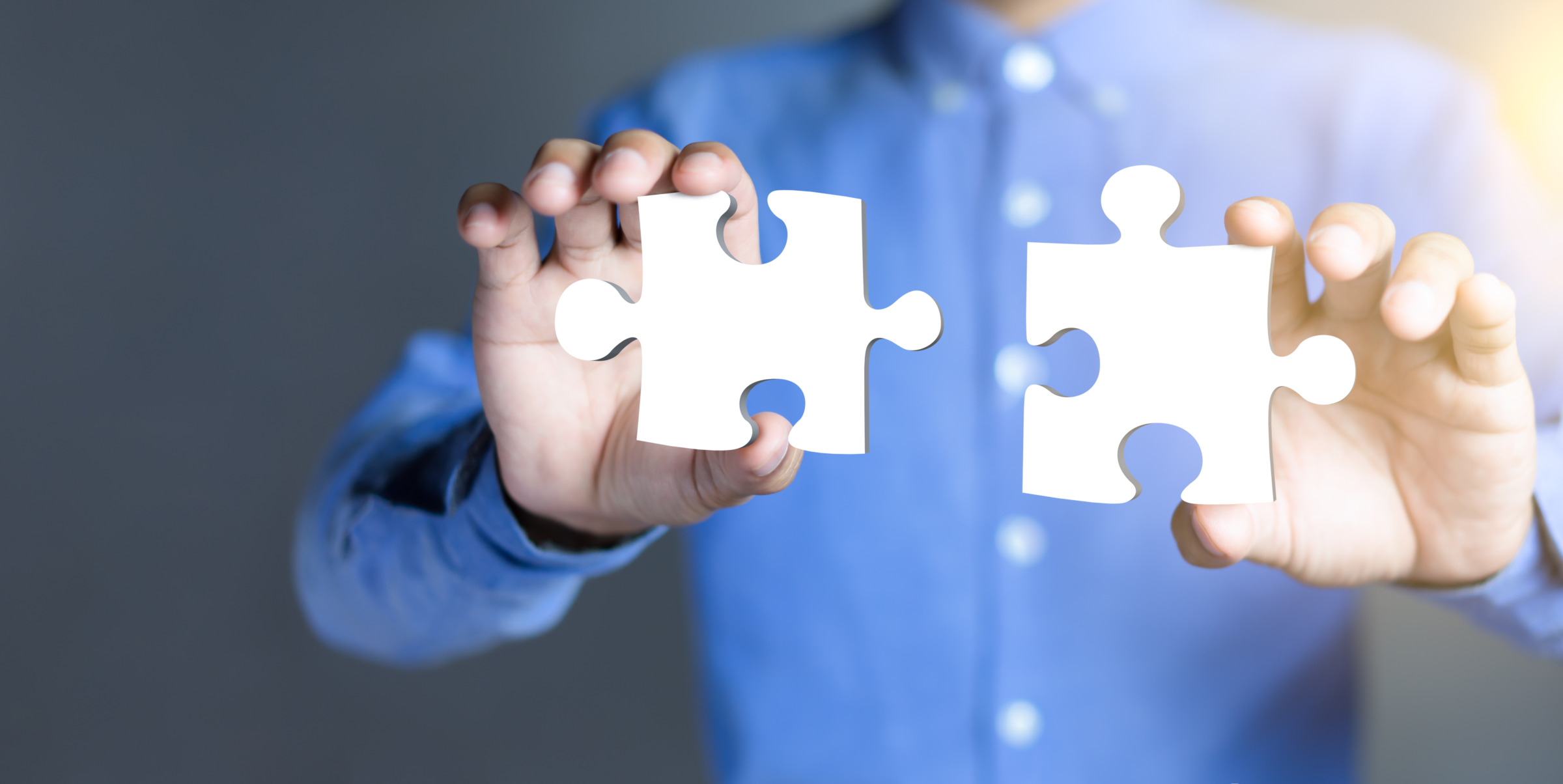 Businessman hands connecting puzzle pieces representing the merging of two companies or joint venture, partnership, Mergers and acquisition concept.